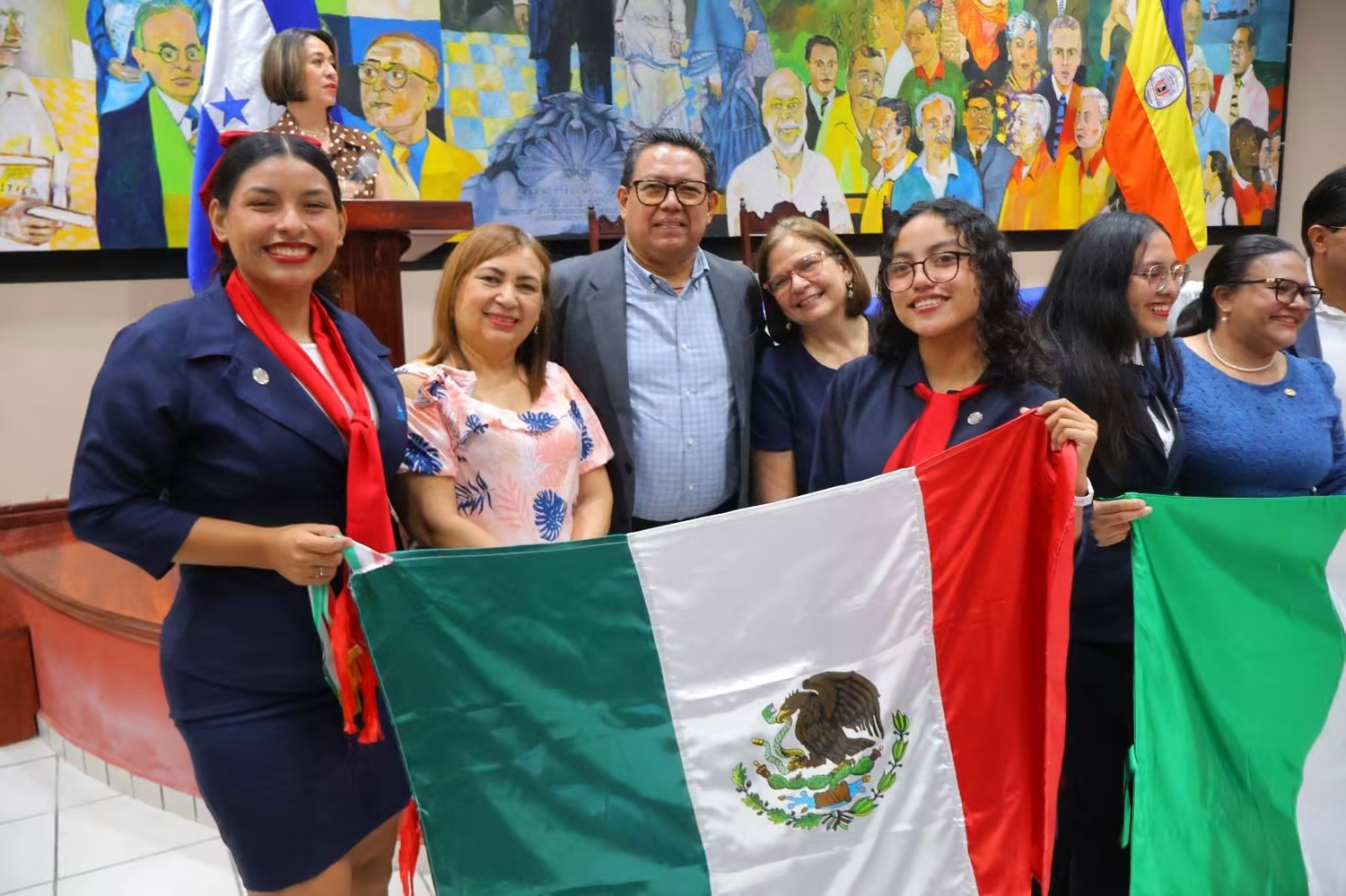 Participantes de la apertura del intercambio académico, frente a un mural y con banderas